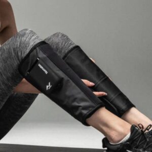 A person wearing athletic leggings and trainers sits with the Normatec Lower Legs compression sleeves on their calves.