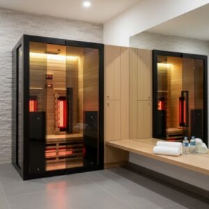 A modern changing room featuring the Infrared Sauna 130 with red glowing panels, a bench stocked with towels and water bottles, and sleek light wood cabinetry.