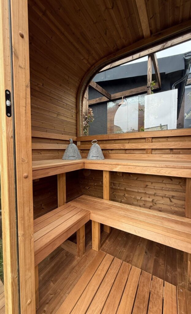 Interior of a wooden sauna with bench seating and two stone sauna buckets on the upper bench, featuring curved walls and a glass door for a relaxing sauna experience.
