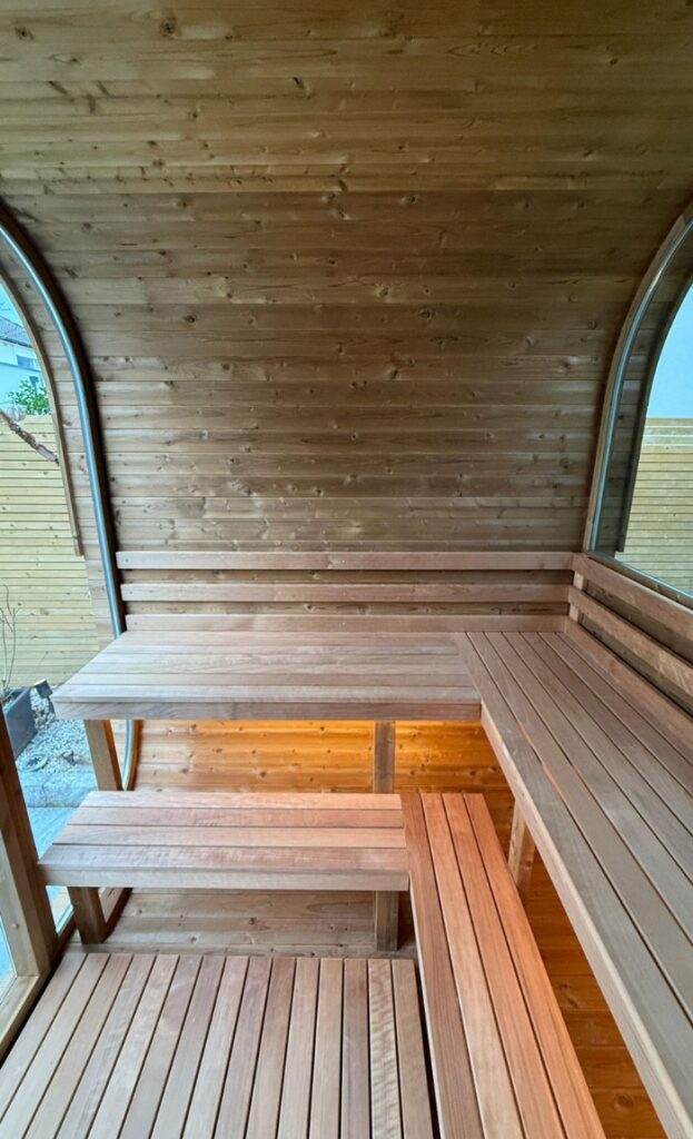 Cosy sauna interior with wooden benches and a table, featuring curved walls and large windows that offer relaxing views of the outdoor area.