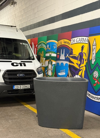 A white van is parked beside a colourful mural with Irish crests, celebrating the GAA spirit of the All-Ireland Final; a large empty grey planter sits in front.